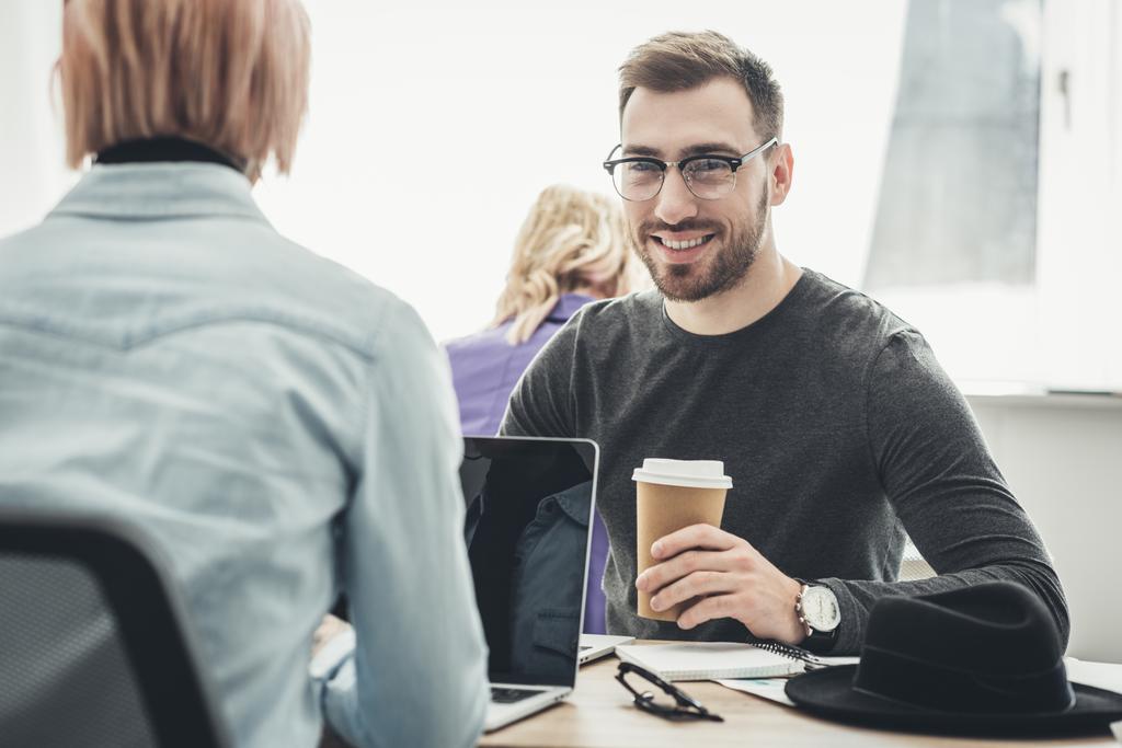 selectieve aandacht van lachende zakenman in brillen met koffie te gaan op de werkplek op kantoor - Foto, afbeelding