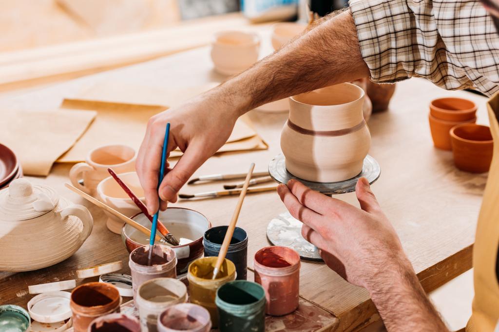 bijgesneden weergave van mannelijke potter schilderij keramiek serviesgoed in werkplaats - Foto, afbeelding