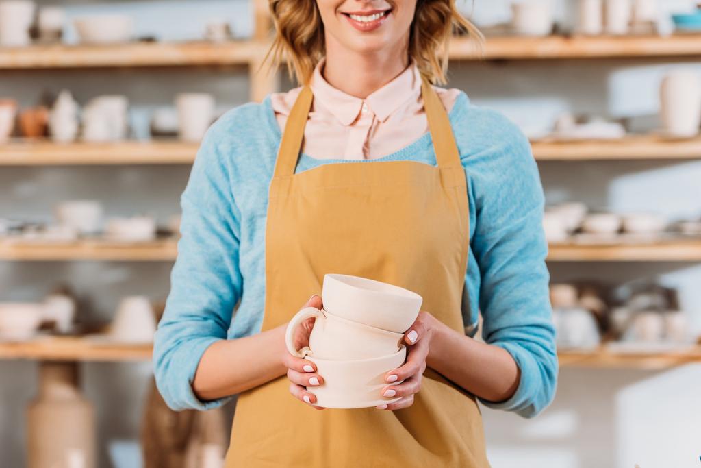 cropped view of potter in apron holding ceramic bowls - Photo, Image