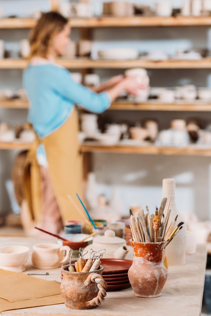 enfoque selectivo del alfarero en el taller con cerámicas y pinceles en primer plano
 - Foto, Imagen