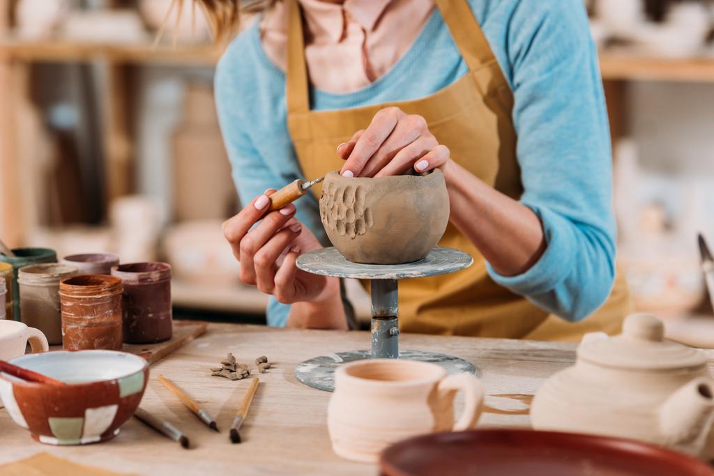 обрезанный вид гончара в фартуке украшения керамической чаши в мастерской
  - Фото, изображение