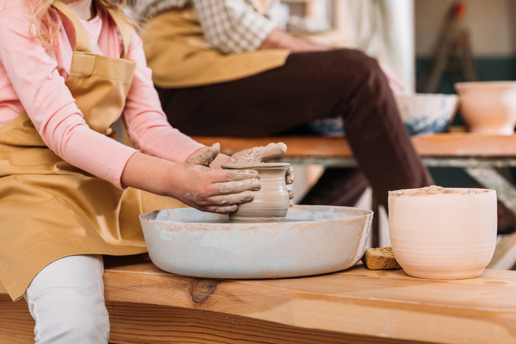 Zugeschnittene Ansicht eines Kindes, das in Werkstatt mit Lehrer Keramiktopf herstellt - Foto, Bild