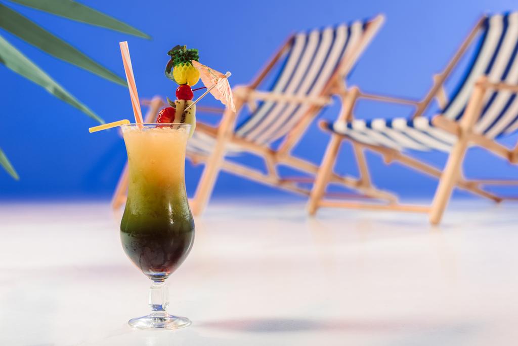 Glass with tropical cocktail by deck chairs on blue background - Photo, Image