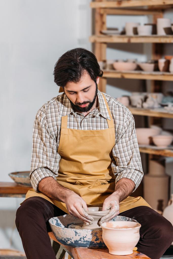 бородатый гончар делает керамический горшок на гончарном круге в мастерской
 - Фото, изображение