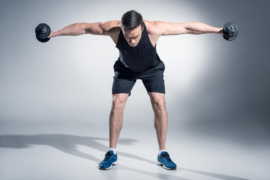 Vonzó férfi sportoló emelő súlyzók a szürke háttér - Fotó, kép