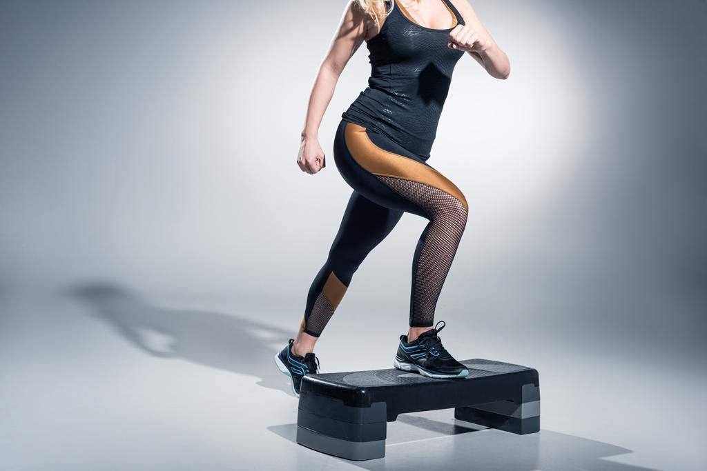 Young woman exercising on step platform on grey background - Photo, Image