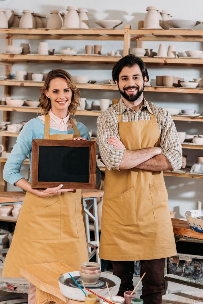 dva vlastníci drží tabuli v keramické dílně s keramikou na policích - Fotografie, Obrázek
