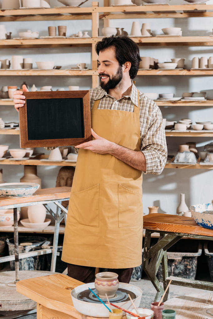 smiling male owner holding chalkboard in pottery workshop - Photo, Image