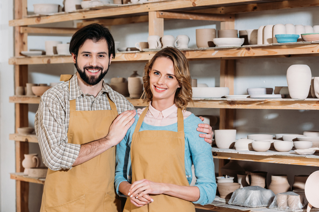 couple dans des tabliers étreignant dans un atelier de poterie avec de la céramique sur des étagères
 - Photo, image