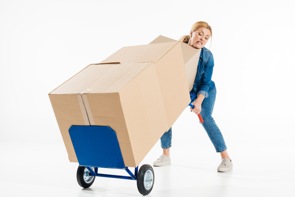 Attractive woman trying to push delivery cart with boxes isolated on white - Photo, Image