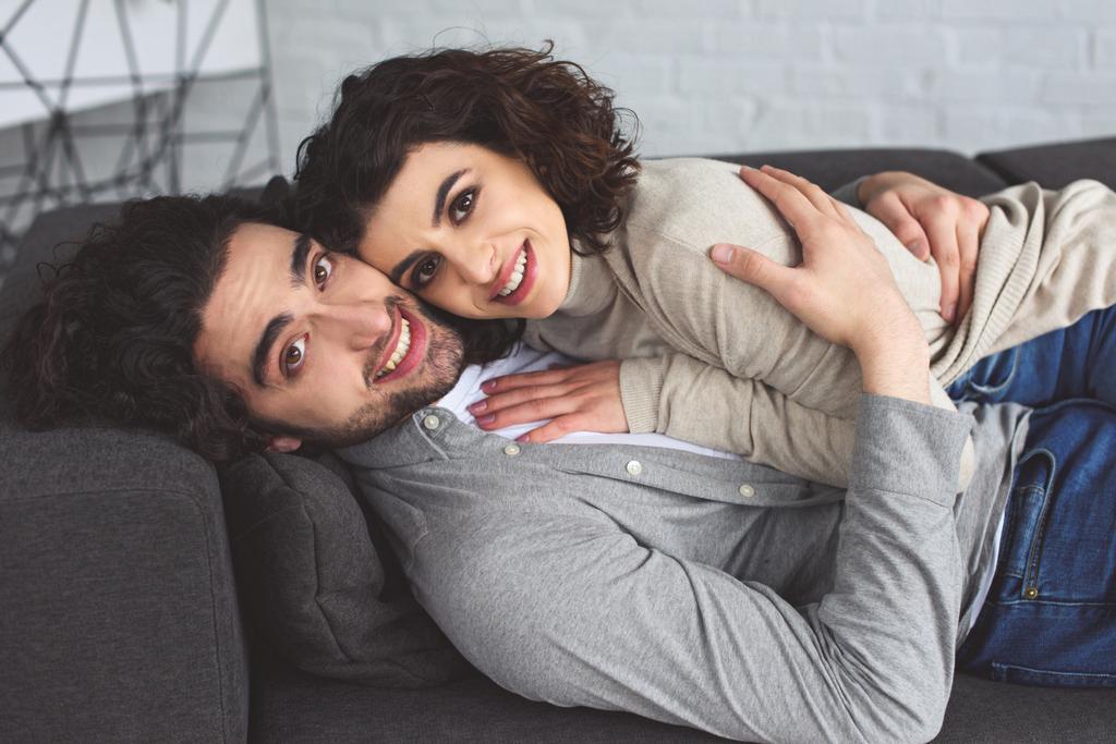 sorridente giovane coppia abbracciare e sdraiarsi sul divano a casa
 - Foto, immagini