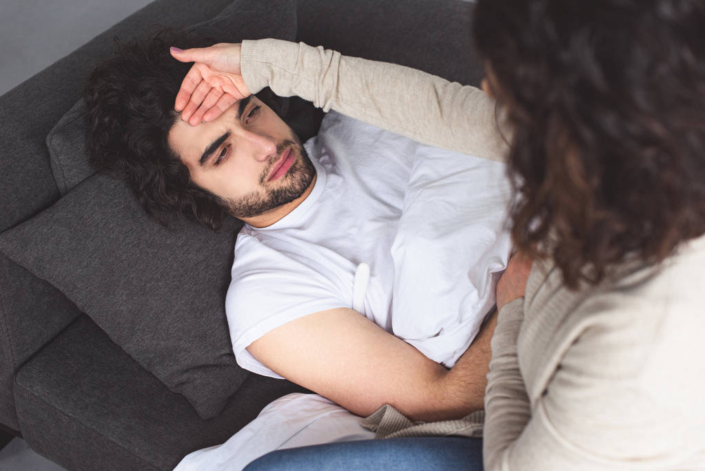 high angle view of girlfriend touching sick boyfriend forehead at home - Photo, Image