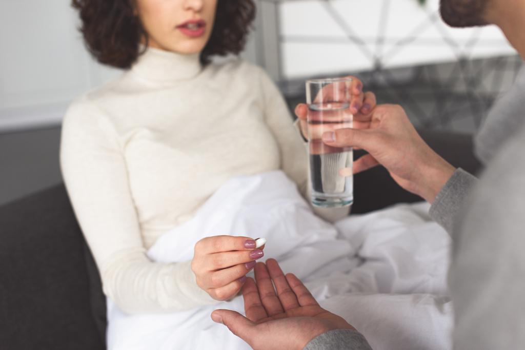 imagem cortada de namorado dando pílula e vidro de água para namorada doente em casa
 - Foto, Imagem