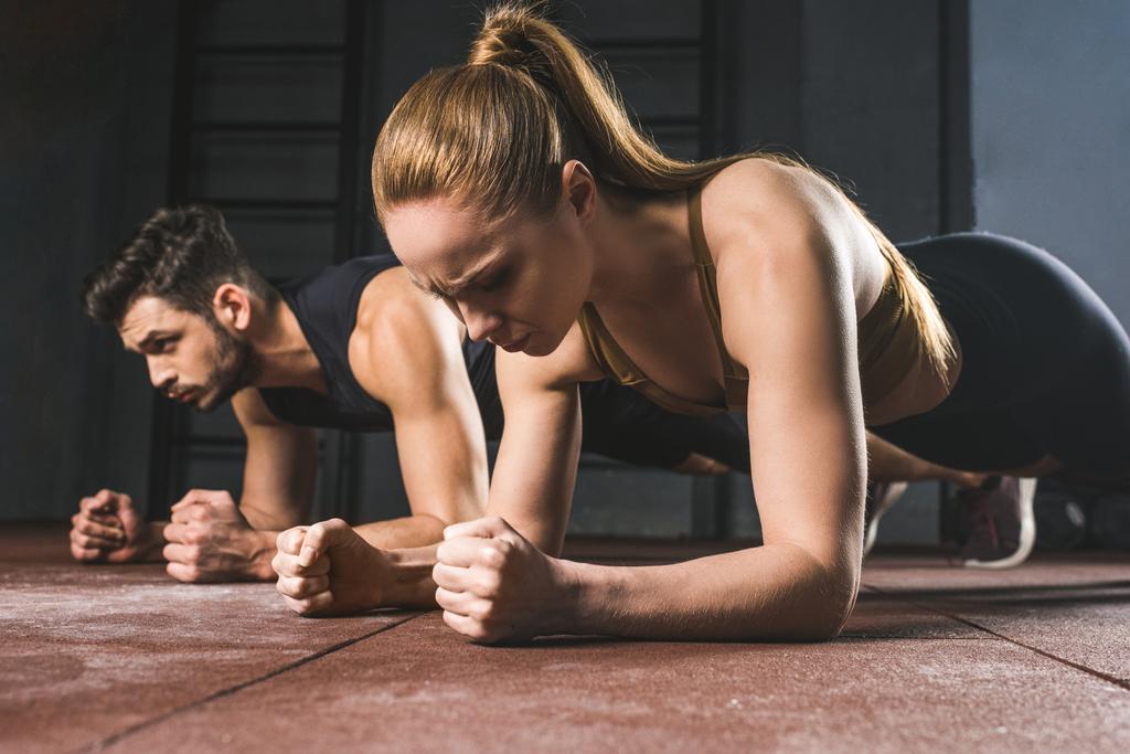 Young sportswoman and sportsman doing plank in gym - Photo, Image