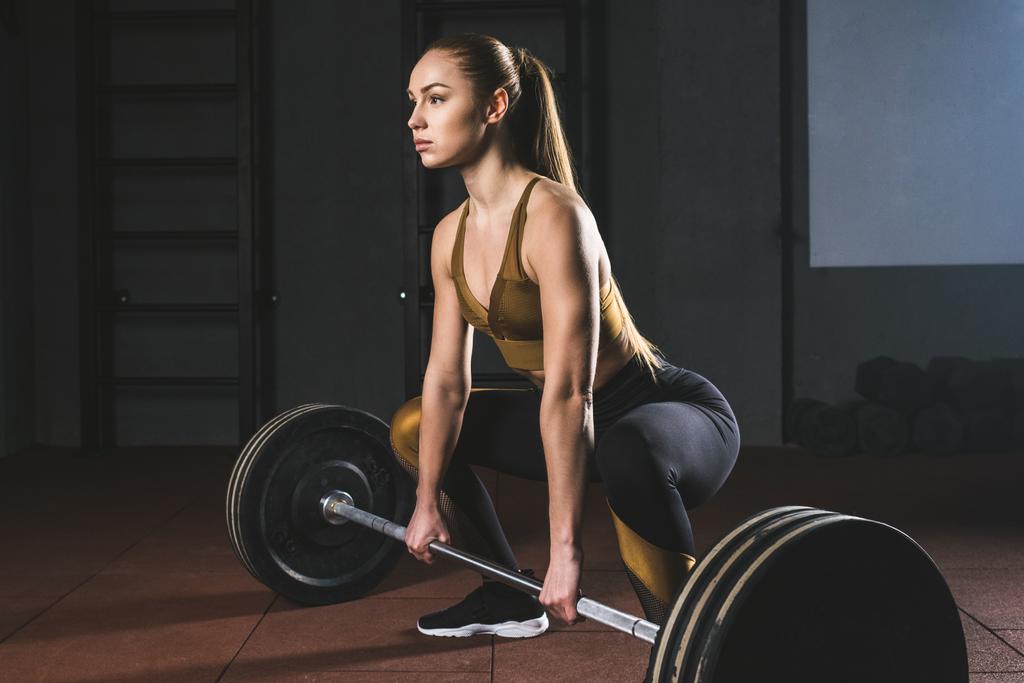 Side view of young sportswoman preparing to raise barbell in gym - Photo, Image