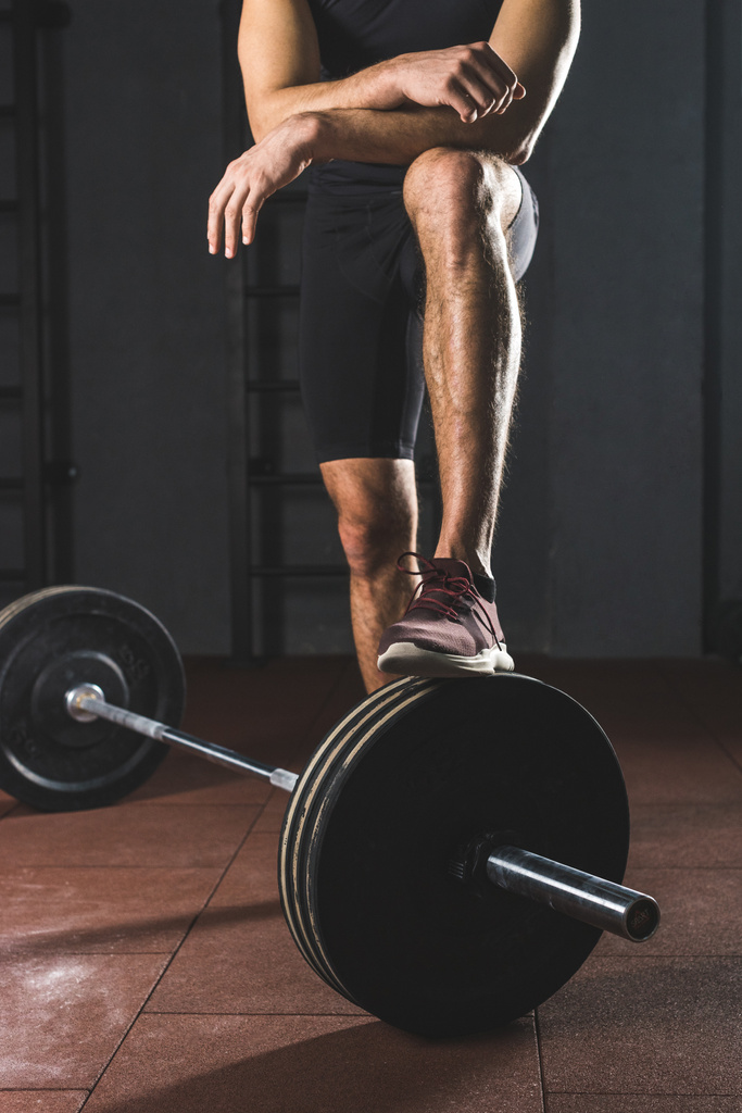 Περικομμένη εικόνα της ανάπαυσης αθλητής που στέκεται στο barbell στο γυμναστήριο - Φωτογραφία, εικόνα