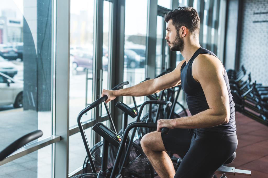 Μερική άποψη του νεαρός αθλητής κάνει προπόνηση στο ποδήλατο άσκησης στο αθλητικό κέντρο - Φωτογραφία, εικόνα