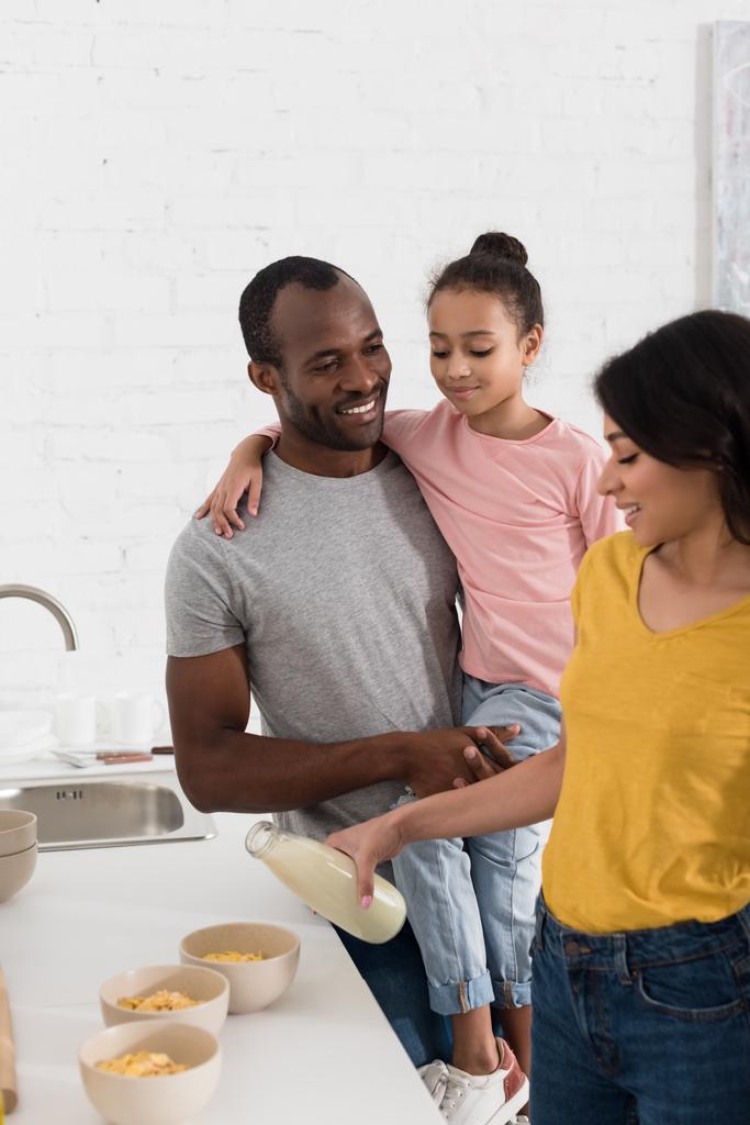 young family pouring milk into cereal breakfast at kitchen - Photo, Image