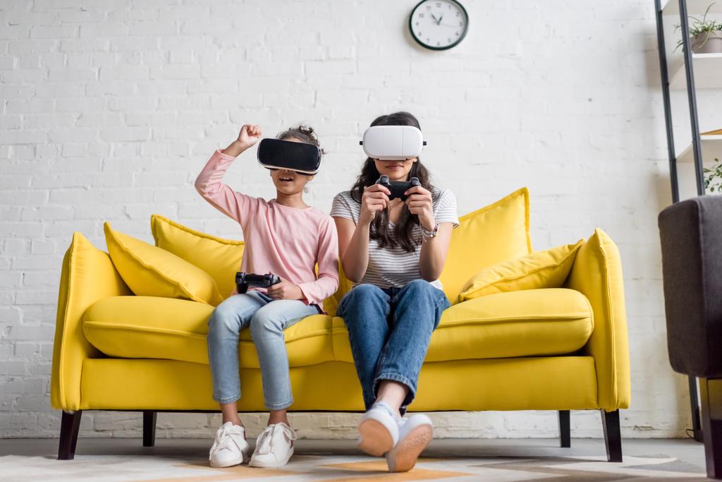 Mutter und Tochter in vr-Headsets beim Spielen von Videospielen zu Hause auf der Couch - Foto, Bild
