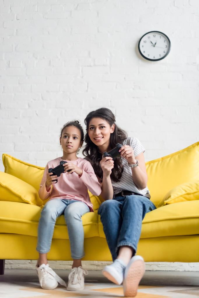 emocional joven madre e hija jugando videojuegos en casa en el sofá
 - Foto, Imagen