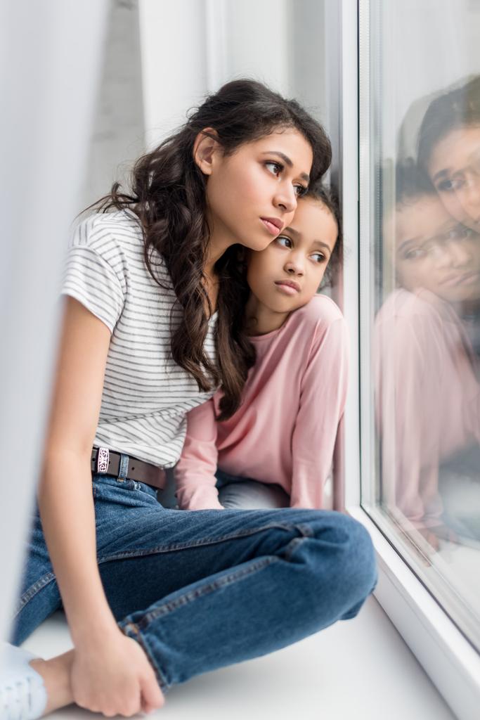 θλιβερή μητέρα και κόρη, κοιτάζοντας μέσα από το παράθυρο - Φωτογραφία, εικόνα