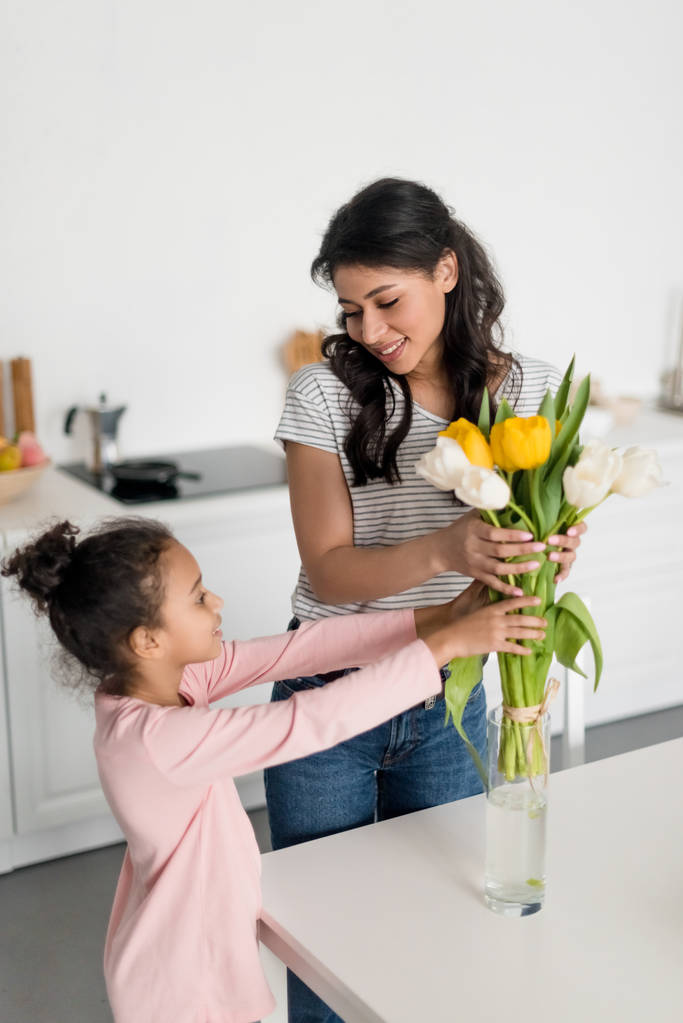 jonge moeder en mooie dochter brengen bloemen in vaas - Foto, afbeelding