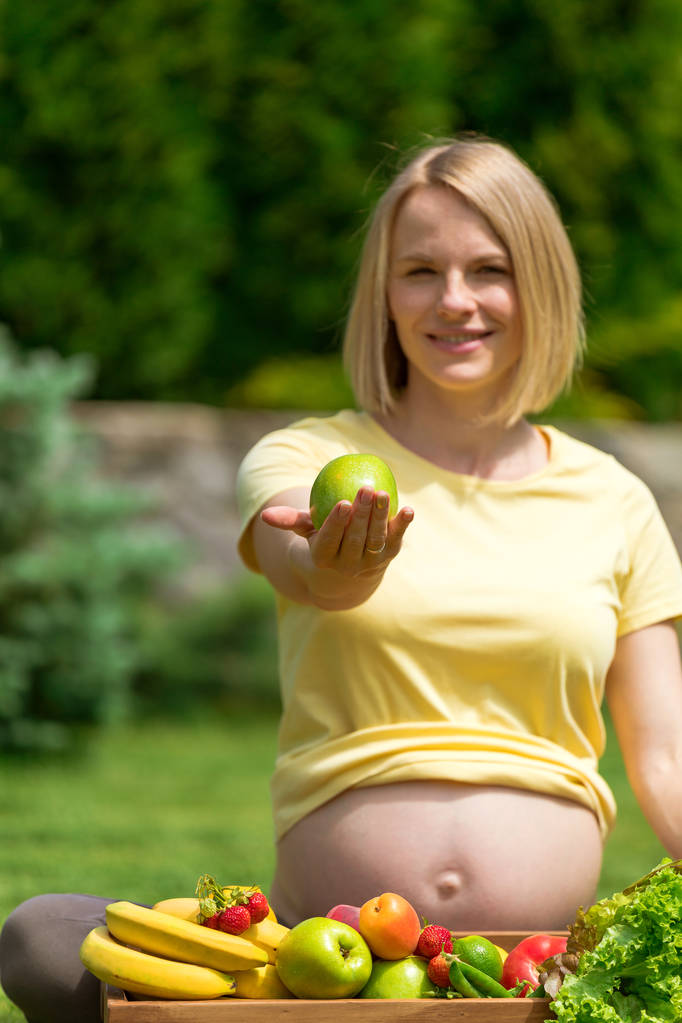Donna incinta seduta sull'erba e che tiene la mela in mano
 - Foto, immagini