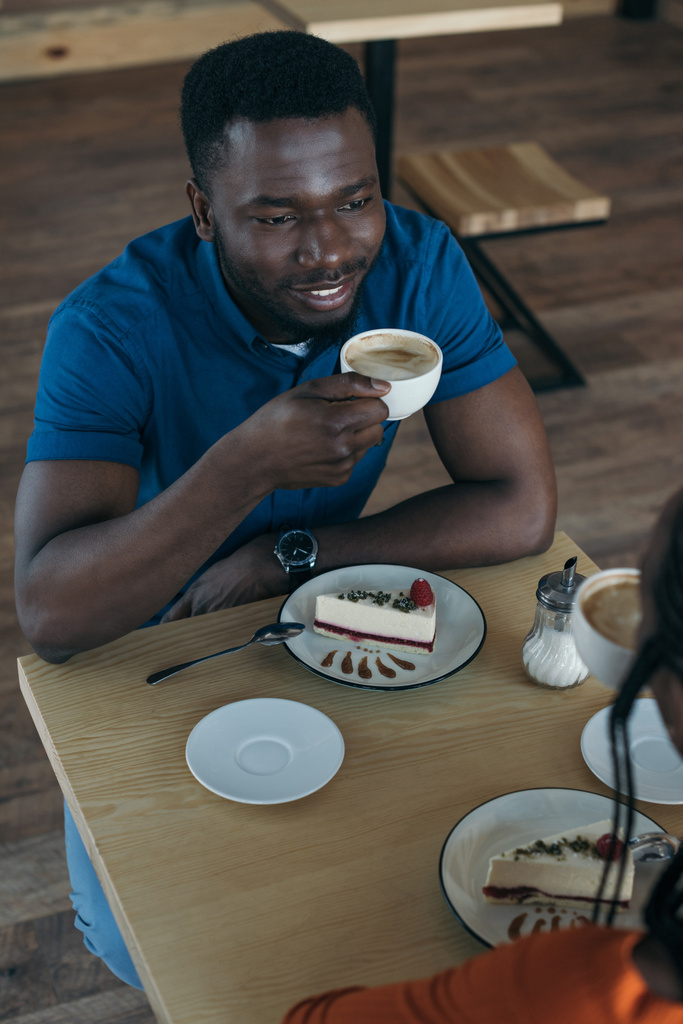 コーヒー ショップでのガール フレンドを見てコーヒーのカップでアフリカ系アメリカ人の笑顔ハイアングル - 写真・画像