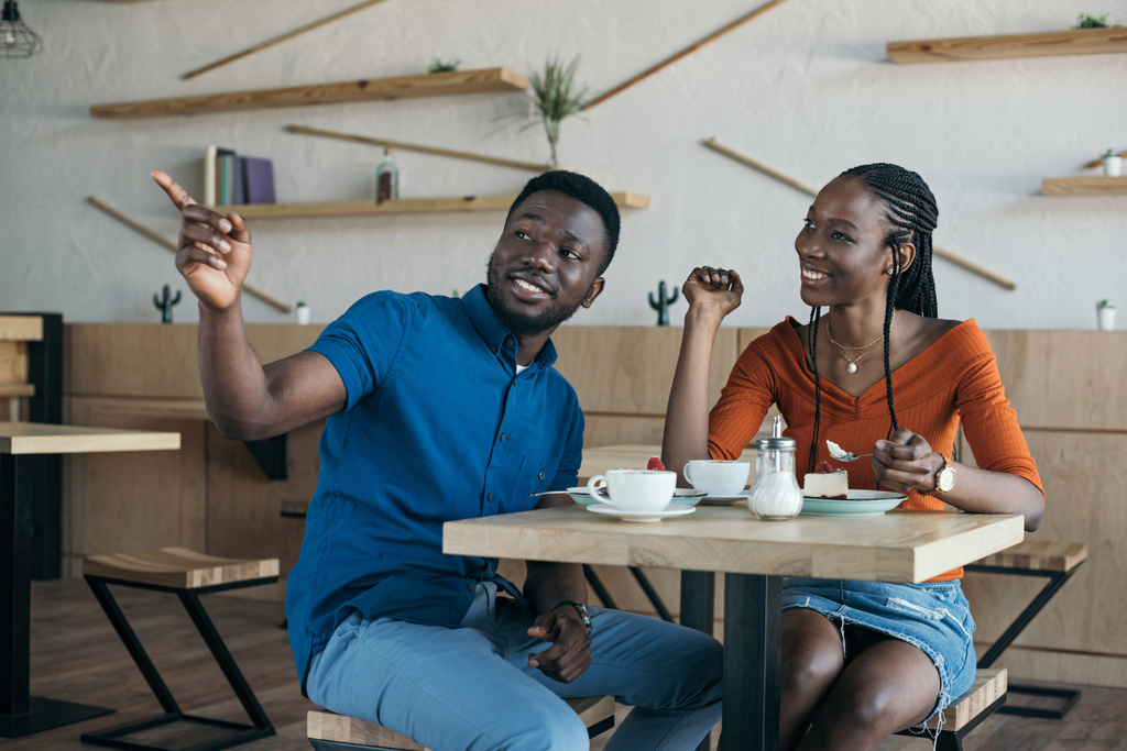 Αφρικανική αμερικανική ζευγάρι κάθεται στο τραπέζι με τα κύπελλα του καφέ και επιδόρπια στο café - Φωτογραφία, εικόνα