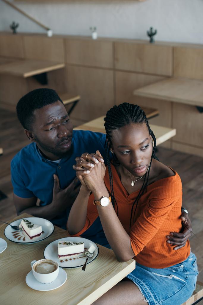 hoge hoekmening van beledigd african american vrouw met vriendje zittend aan tafel in café - Foto, afbeelding