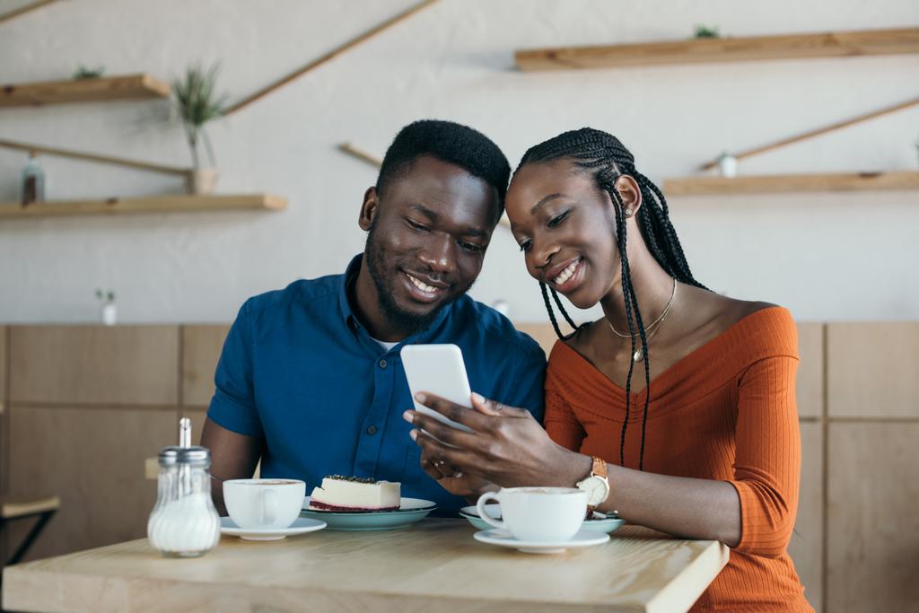χαρούμενα αφρικανική αμερικανική ζευγάρι χρησιμοποιώντας smartphone μαζί σε καφενείο - Φωτογραφία, εικόνα