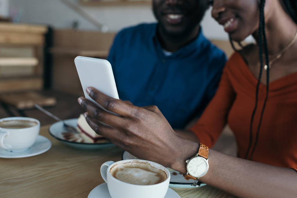περικοπεί το πλάνο της αφρικανική αμερικανική ζευγάρι χρησιμοποιώντας smartphone μαζί σε Cafe - Φωτογραφία, εικόνα