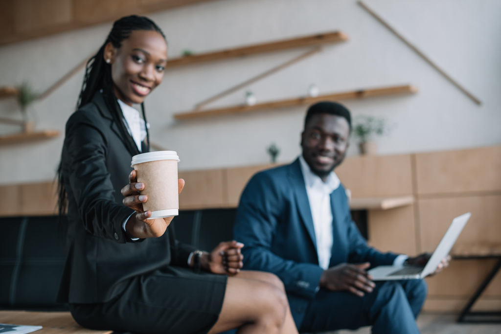 foco seletivo de sorrir empresário afro-americano com laptop e colega mostrando café para se aproximar no café
 - Foto, Imagem