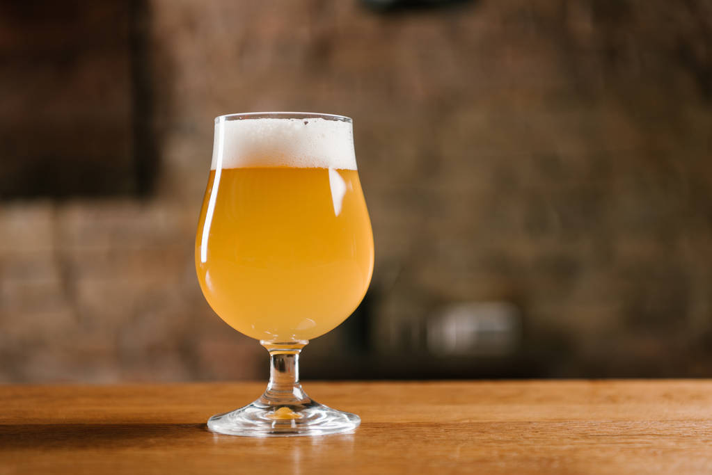 вкусное свежее пиво с пеной в стекле на деревянном столе в баре
 - Фото, изображение