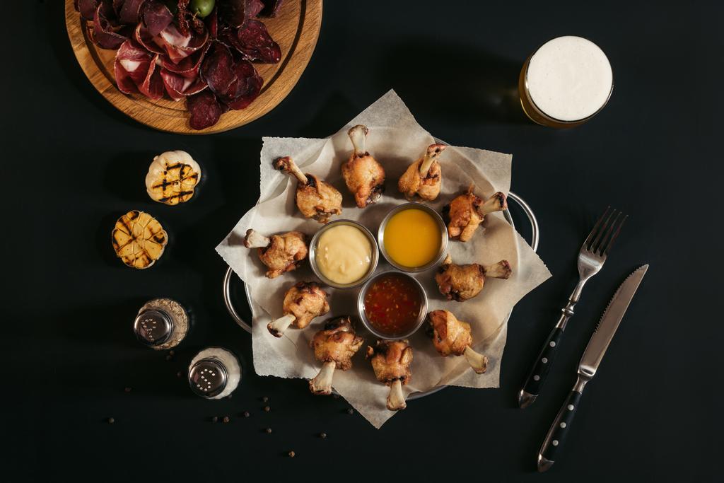 τηγανητό κοτόπουλο με σάλτσες, καρυκεύματα, ποτήρι μπύρας και γκουρμέ ανάμικτες σκάφη κρέας σε μαύρο  - Φωτογραφία, εικόνα