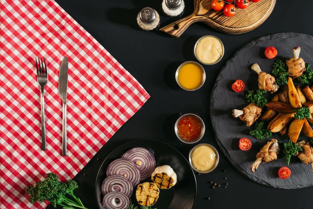 黒の市松模様のナプキンとフォークとナイフ、野菜、ソースとチキンおいしいロースト ポテトのトップ ビュー  - 写真・画像