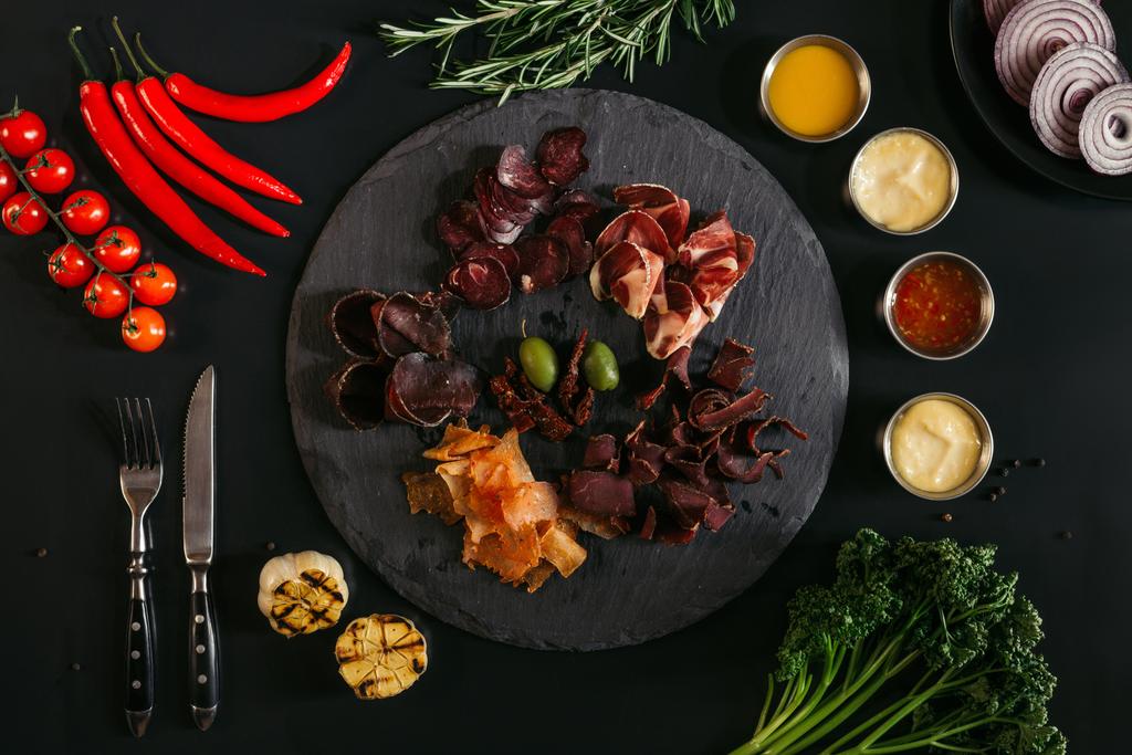 pohled shora gurmánské míchané maso na břidlicové desky, různé omáčky a zeleniny na černém pozadí - Fotografie, Obrázek