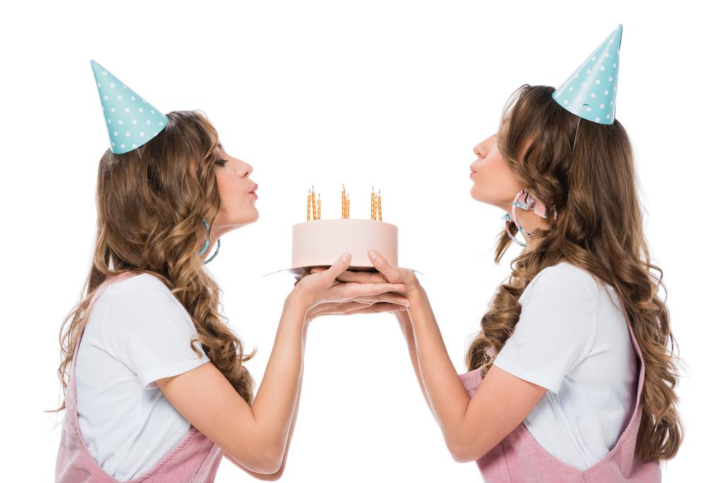 side view of beautiful young twins blowing out candles on birthday cake isolated on white - Photo, Image