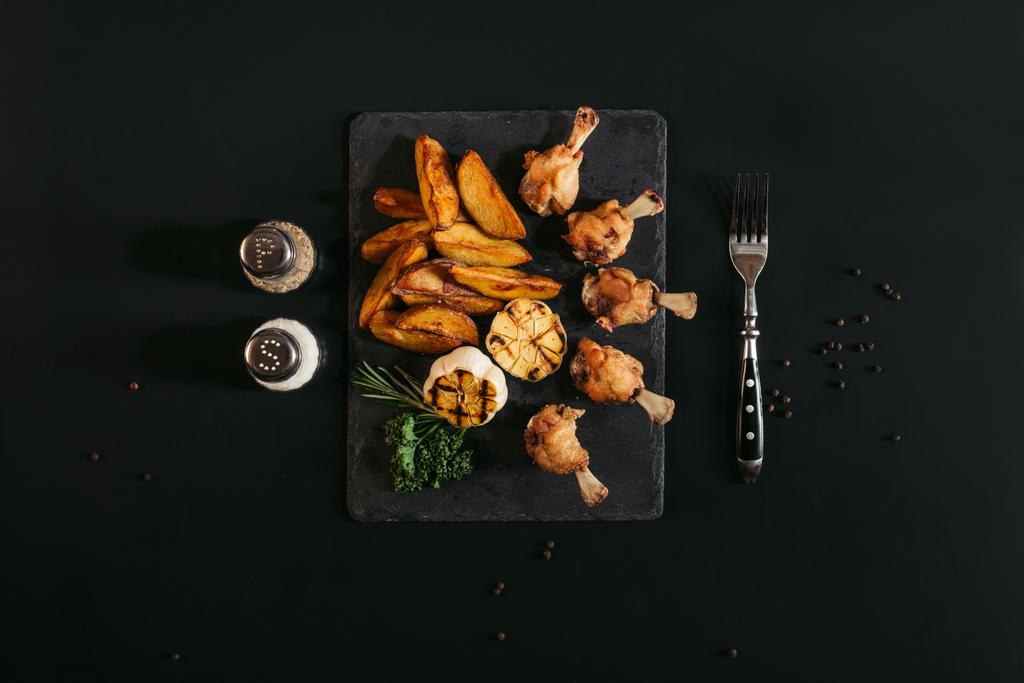 黒のスレート板でおいしいロースト ポテト鶏と焼きニンニクのトップ ビュー  - 写真・画像