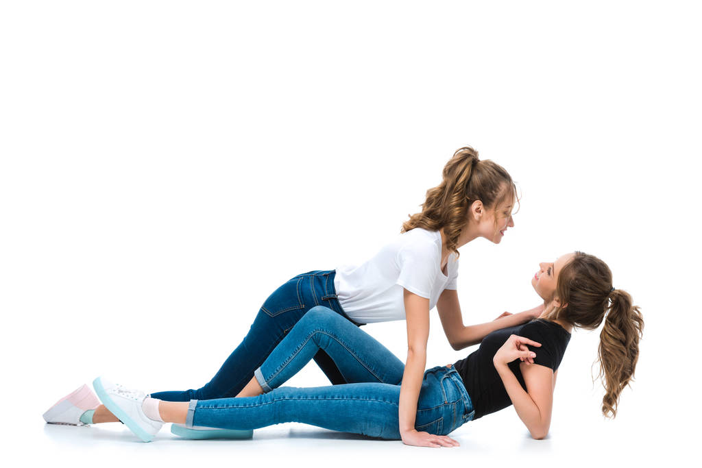 Zijaanzicht van aantrekkelijke jonge twin knuffelen liggend op de vloer zus op wit - Foto, afbeelding