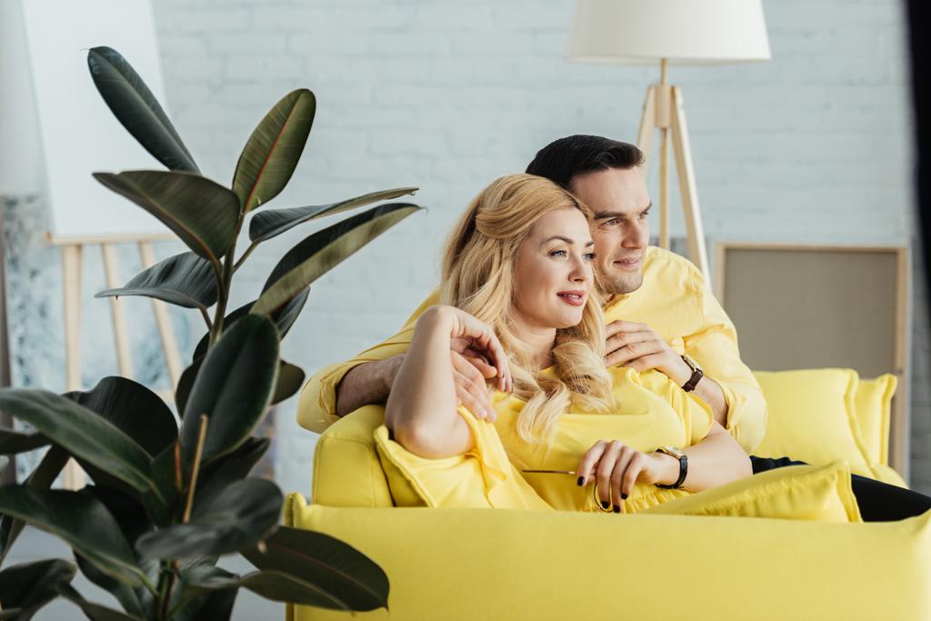 Mooie paar zitten op gele sofa in lichte kamer - Foto, afbeelding