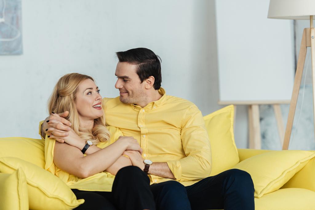 Bonita pareja mirándose y sentada en un sofá amarillo
 - Foto, imagen