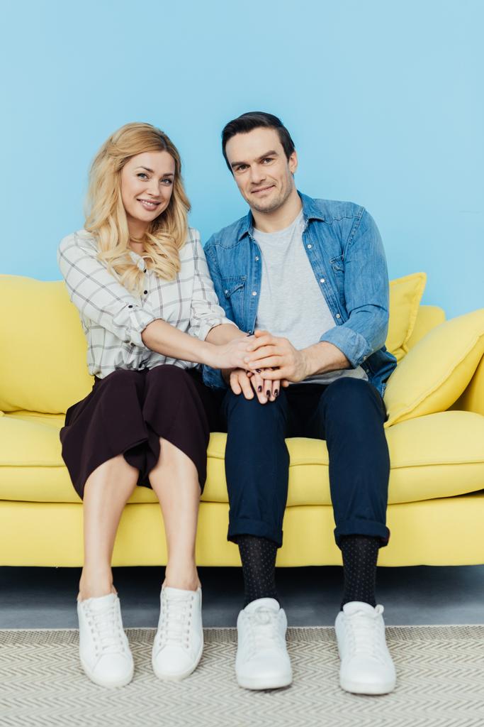 Feliz pareja sentada y cogida de la mano en un sofá amarillo
 - Foto, imagen