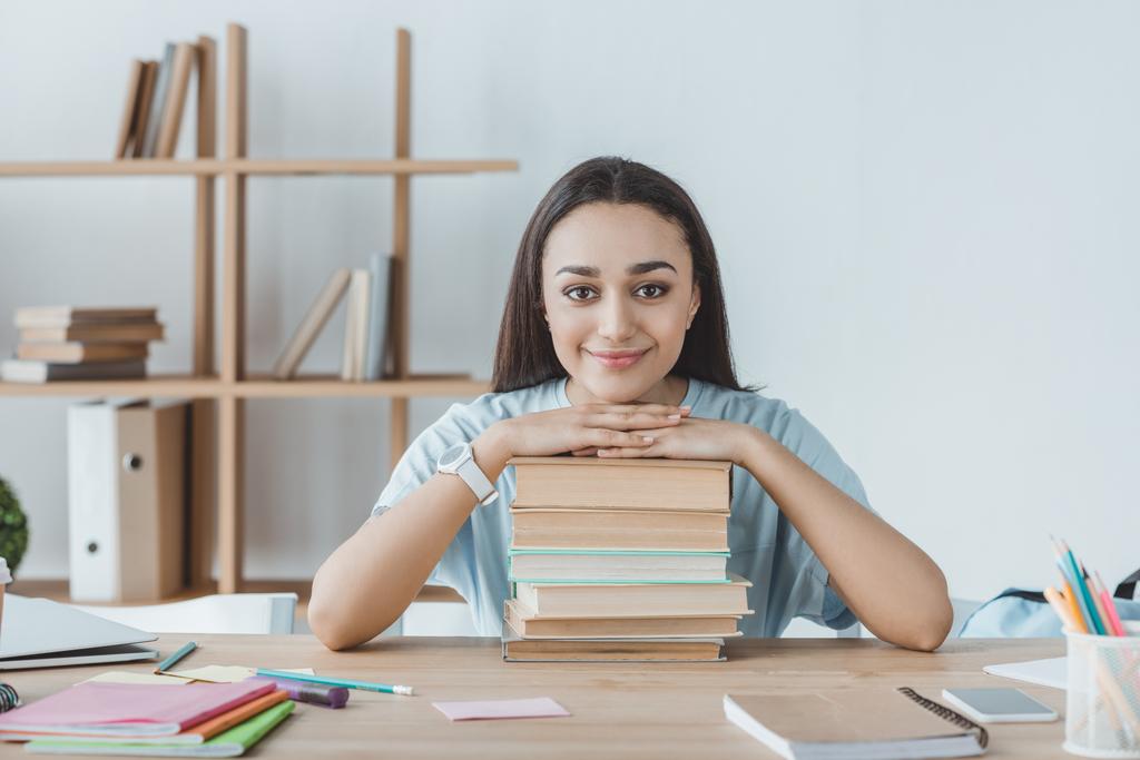 smiling mixed race girl sitting at table with books  - Photo, Image