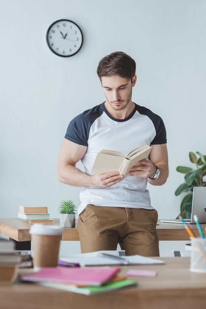 mannelijke student studeert met boek in kamer met copybooks - Foto, afbeelding