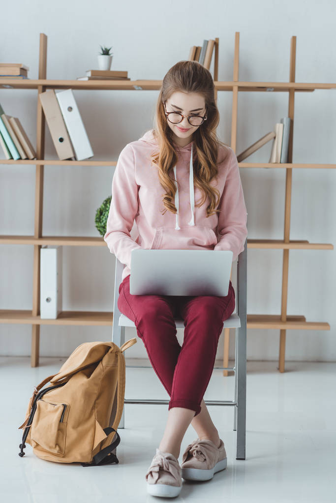 ξανθιά φοιτητής κάθεται με σακίδιο και να χρησιμοποιούν φορητό υπολογιστή - Φωτογραφία, εικόνα