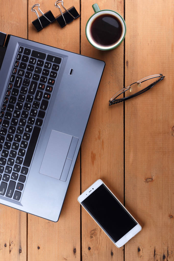 Laptop a šálku kávy na dřevěné pozadí, pracovní stanice na starý stůl, smartphone a notebook, pero a brýle na pracovišti, značkové pracovní stanice, umění - Fotografie, Obrázek
