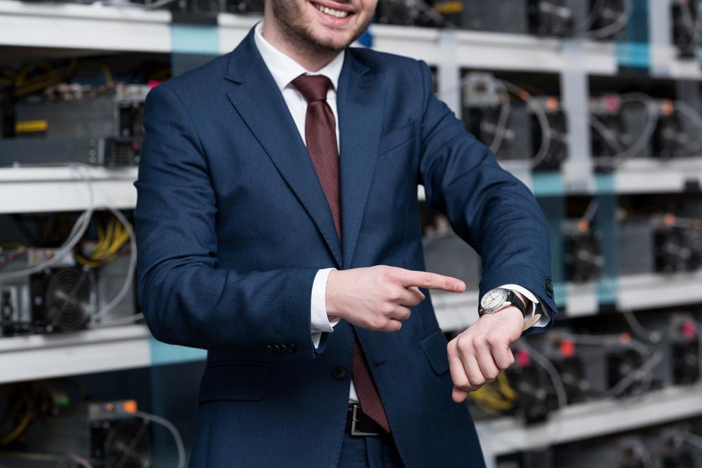 Schnappschuss eines lächelnden Geschäftsmannes, der auf die Armbanduhr der Minenfarm von Ethereum zeigt - Foto, Bild