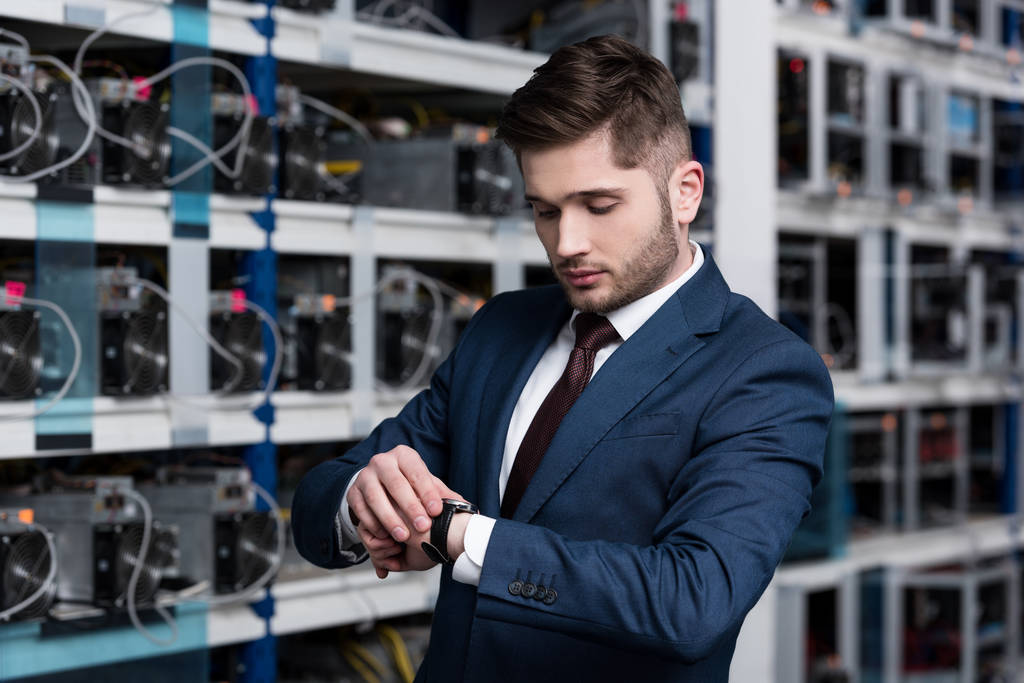 handsome young businessman looking at wristwatch at ethereum mining farm - Photo, Image