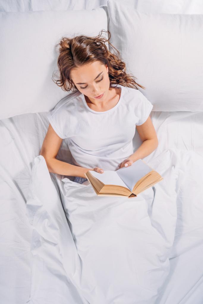 vista aerea di focalizzata giovane donna lettura libro a letto
 - Foto, immagini